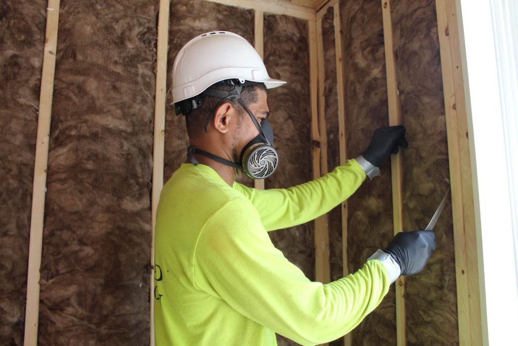 An Advanced Green worker installs fiberglass insulation on a building wall