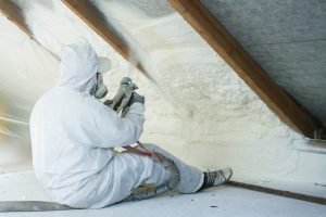 A worker installing spray-foam insulation on an attic ceiling