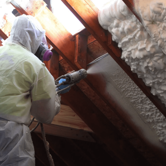 A worker uses a pump to apply spray foam insulation to a roof's inside