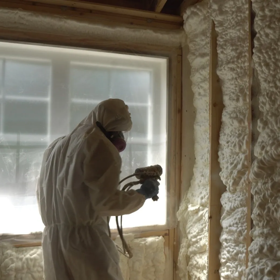 A person using a spray gun to install insulation in a home. They are wearing all white protective gear