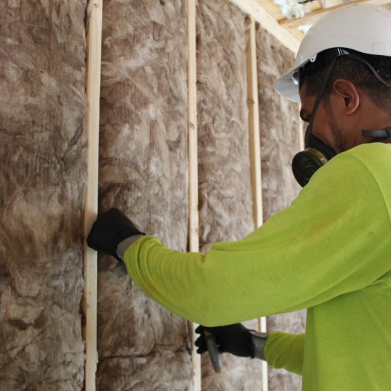 An Advanced Green worker installs fiberglass insulation on a building wall