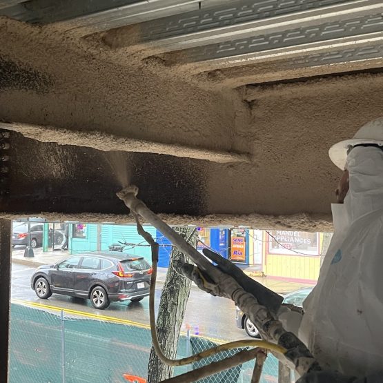 A worker uses a brush to spread fireproof insulation around a building's structure